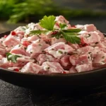 A creamy bowl of ham salad with celery, onions, and relish served with crackers and garnished with fresh parsley